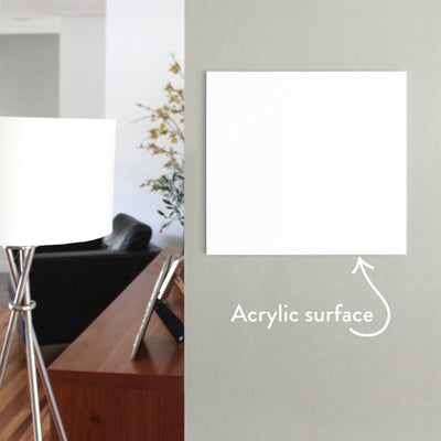 A modern room with minimalist design showcases a Girl Friday Shop White Acrylic Dry Erase Memo Board on a gray wall, labeled with an arrow. A sleek floor lamp with a white shade stands near the board, while a wooden table holding a photo frame contributes warmth to the scene.