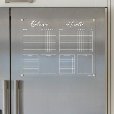 The Girl Friday Acrylic Fridge Chore Chart for 2 children is elegantly displayed on a metallic surface. It includes sections for Olivia and Hunter, daily boxes labeled M, T, W, T, F, S, S to track tasks, and wet-erase markers for easy updating of weekly tasks and notes.