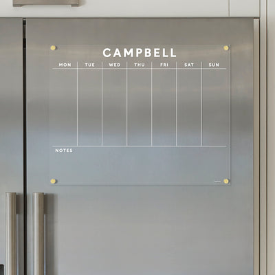The Acrylic Fridge Calendar by Girl Friday Shop, customized with CAMPBELL, elegantly adorns a stainless steel refrigerator. It features days of the week labeled in white and offers ample space for notes at the bottom, ideal for use with wet-erase markers.