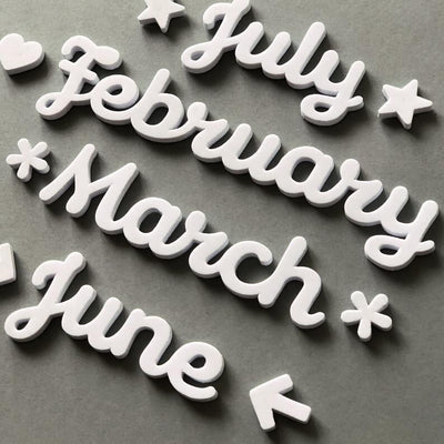 The Girl Friday Shops Magnetic Month Words feature stylish white cutout text for July, February, March, and June. With stars, hearts, and arrows adorning the design, these high-density foam accessories elegantly enhance any gray surface.