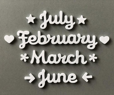 White cursive words spelling July, February, March, and June on a gray background feature stars, hearts, or arrows. Ideal as Girl Friday Shops Magnetic Month Words to stylishly enhance your calendar.