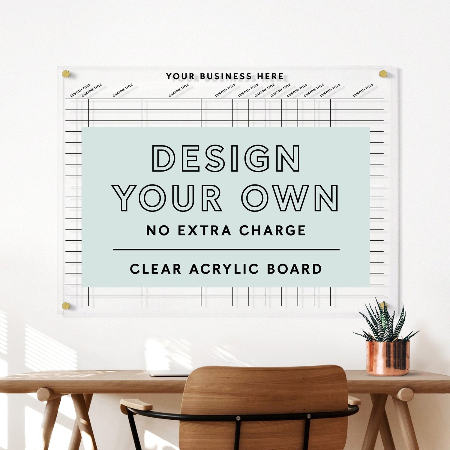 A room with a wooden chair, desk, and potted plant boasts a large wall-mounted Design Your Own Acrylic Tracking Board | Horizontal by Girl Friday Shop. Perfect for creativity with wet-erase markers, it features the text: Design Your Own - No Extra Charge.