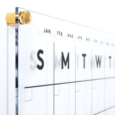 The Girl Friday Shops Clear Acrylic Monthly Wall Calendar with Notes | Horizontal is perfect for organizing as a family planner. It features bold weekday letters, abbreviated months, and pairs seamlessly with wet-erase markers, mounted elegantly using gold-colored hardware.
