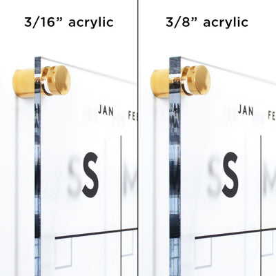 Two acrylic panels with gold standoffs showcase the Girl Friday Shops Clear Acrylic Monthly Wall Calendar with Notes | Horizontal. Labeled 3/16” acrylic (left) and 3/8” acrylic (right), both panels have a visible calendar section for planning using wet-erase markers.