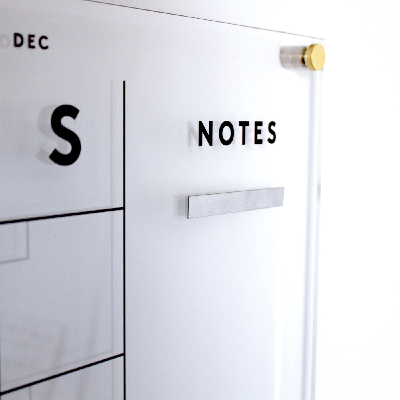 Close-up of a transparent acrylic wall calendar with a minimalistic design using neodymium cube magnets and metallic mounting hardware. The NOTES section, enhanced by Girl Fridays metal strips for magnets, blends functionality with modern elegance.