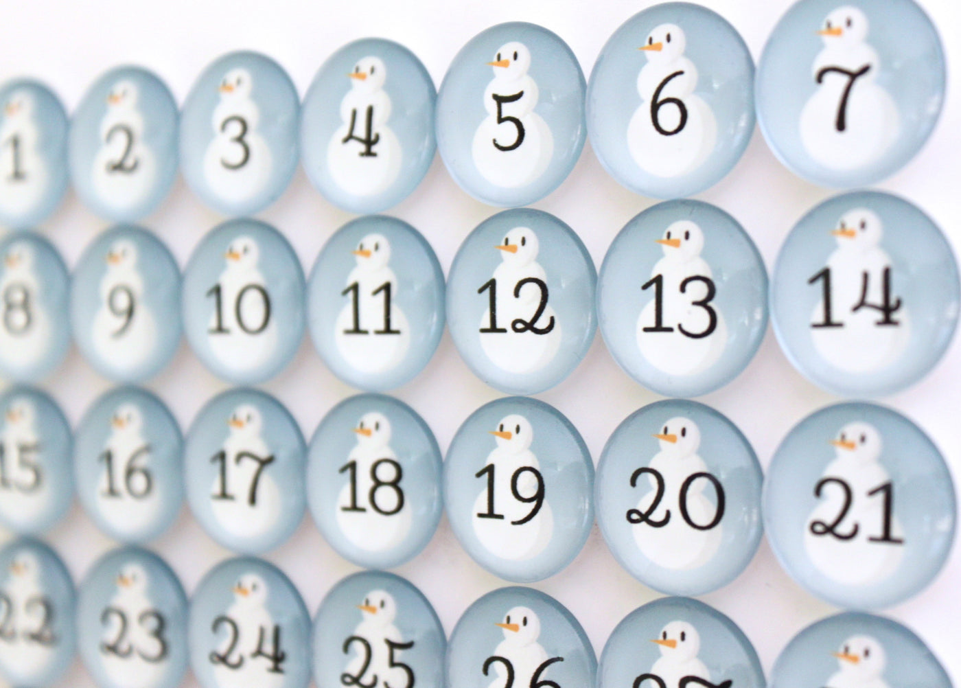 Close-up of Girl Fridays Number Magnets - Snowmen set showing a winter calendar grid of round, light blue magnets with snowmen and black numbers 1 to 42; each Frosty has a tiny orange nose.