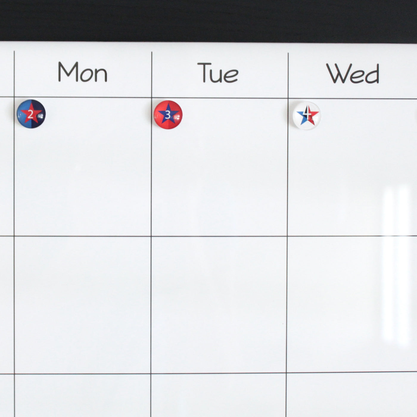 A Girl Friday whiteboard calendar uses Number Magnets - Stars - Patriotic Independence Day from the 4th of July set to show Mon with a 2, Tue with a 3, and a blank red, white, and blue star on Wed, suggesting early July. The rest of the grid is empty.