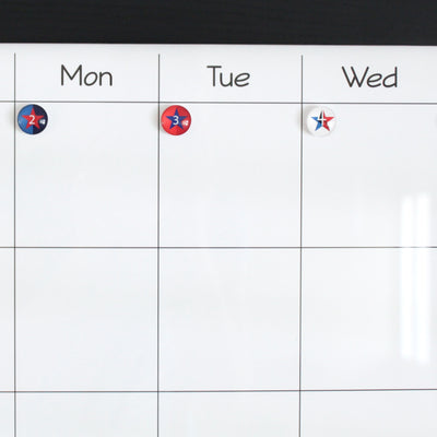 A Girl Friday whiteboard calendar uses Number Magnets - Stars - Patriotic Independence Day from the 4th of July set to show Mon with a 2, Tue with a 3, and a blank red, white, and blue star on Wed, suggesting early July. The rest of the grid is empty.