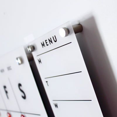 Close-up of the Girl Friday Shop Magnetic Acrylic Menu Board with sections for Monday to Wednesday. MENU is prominently displayed at the top, and its mounted on a white wall using metal pegs.