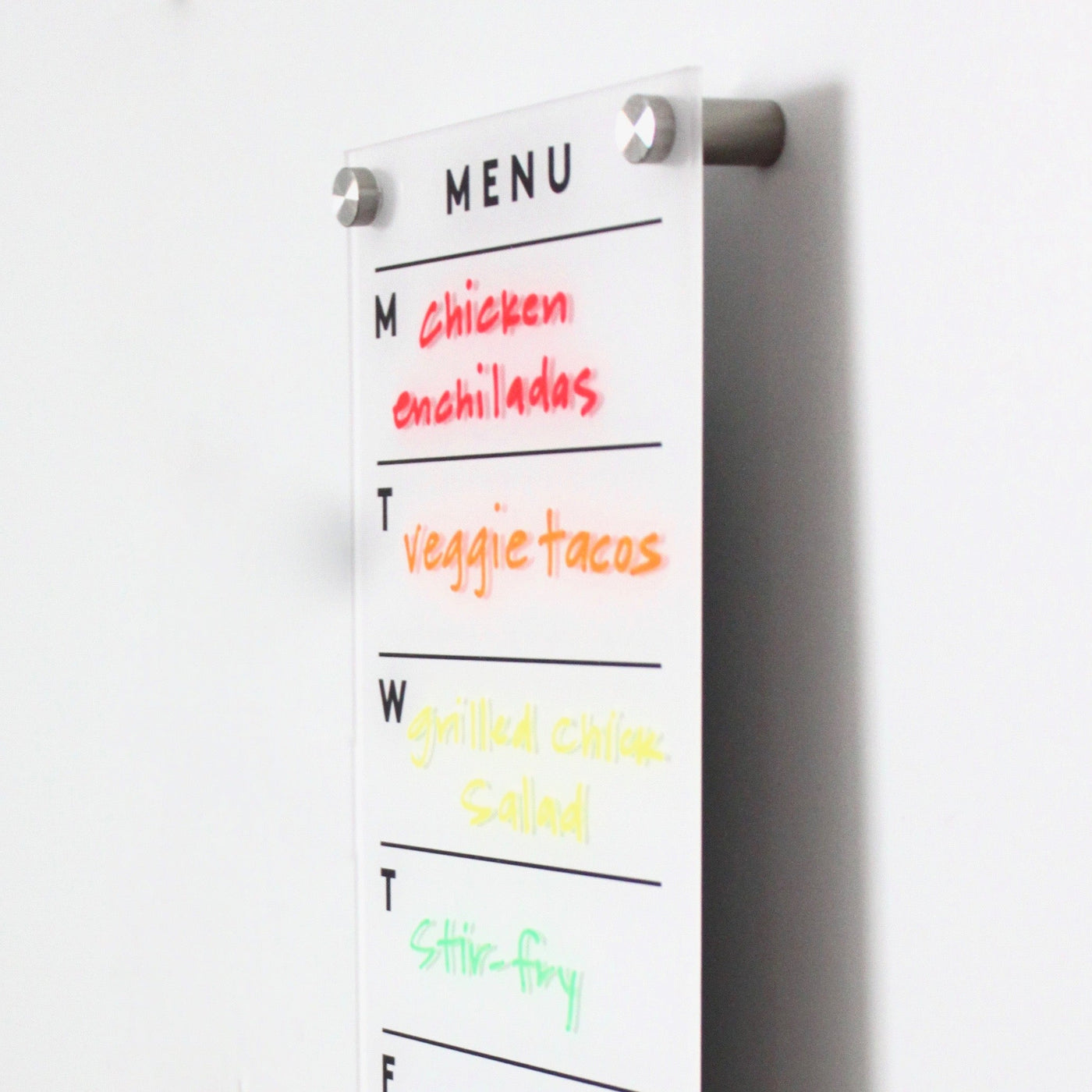 The Girl Friday Shop Magnetic Acrylic Menu Board showcases meals with weekday markers: M (red) for chicken enchiladas, T (orange) for veggie tacos, W (yellow) for grilled chicken salad, and T (green) for stir-fry.