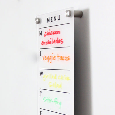 The Girl Friday Shop Magnetic Acrylic Menu Board showcases meals with weekday markers: M (red) for chicken enchiladas, T (orange) for veggie tacos, W (yellow) for grilled chicken salad, and T (green) for stir-fry.