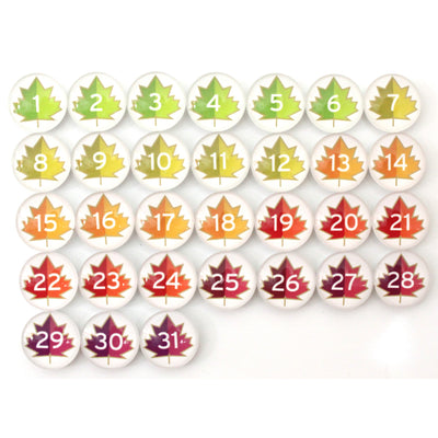 Enhance your home decor with Girl Fridays Number Magnets for September, featuring a grid of buttons numbered 1 to 30 adorned with maple leaf designs in fall colors transitioning from green and yellow to orange, red, and purple, creating a stunning autumn gradient.