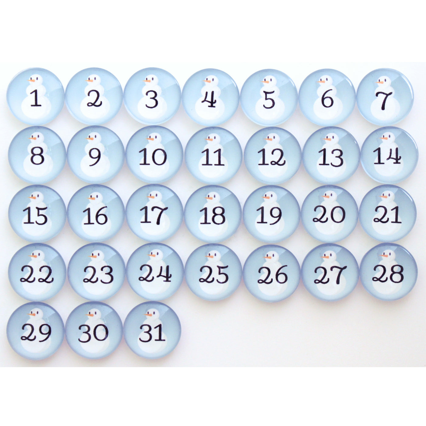 The Girl Friday Number Magnets - Snowmen set includes 31 round, light blue buttons each showing a number from 1 to 31 in black. Topped with a charming cartoon penguin, these magnets evoke the whimsical charm of Frosty the Snow Person.