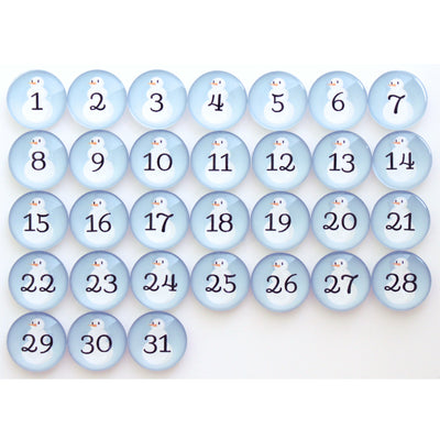The Girl Friday Number Magnets - Snowmen set includes 31 round, light blue buttons each showing a number from 1 to 31 in black. Topped with a charming cartoon penguin, these magnets evoke the whimsical charm of Frosty the Snow Person.
