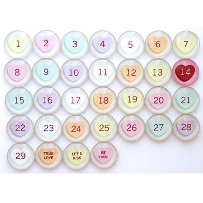 The Girl Friday Number Magnets for February feature candy-shaped buttons, ideal as Valentine magnets. Each pastel button is numbered 1 to 31, with the red 14 standing out. Three buttons read: TRUE LOVE, LETS KISS, and BE TRUE.