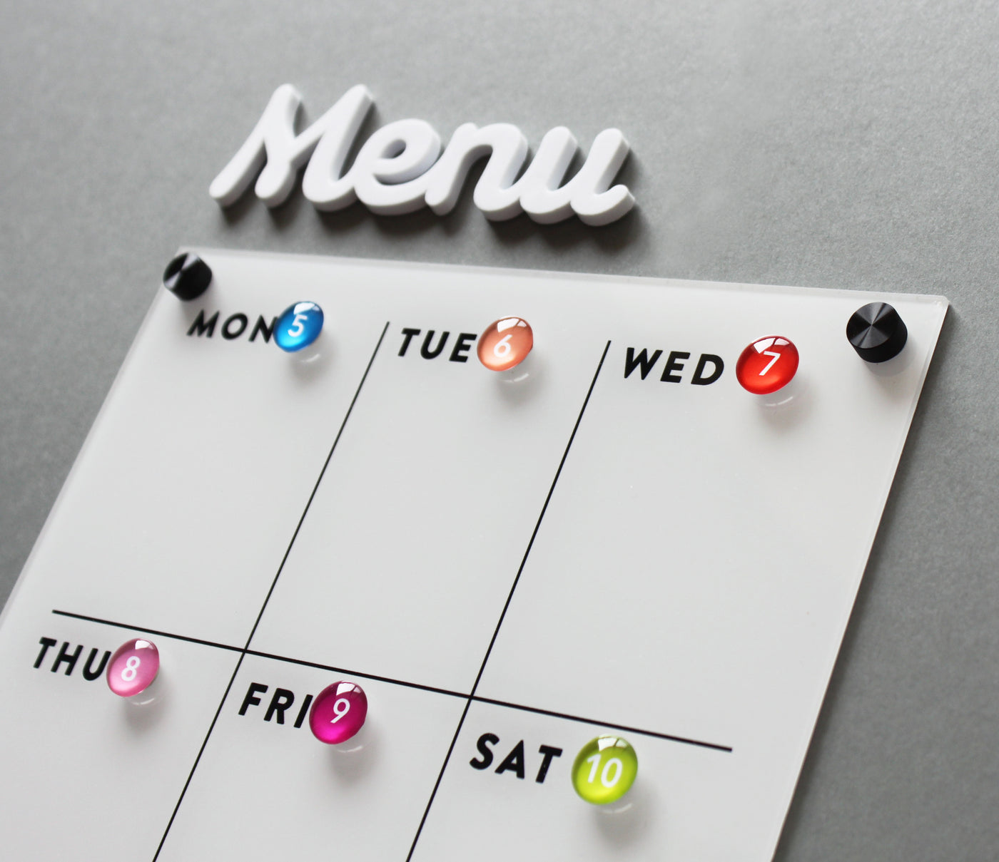 The White Acrylic Weekly Fridge Menu Board with Notes by Girl Friday Shop features a gray background and colored magnets for each day from Monday to Saturday, allowing the showcased schedule on its dry erase surface to stand out against the boards sleek, modern design.