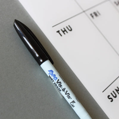 A white Expo Vis-à-Vis wet erase marker with a black cap rests on a gray surface next to a sleek Girl Friday Shop Chore Chart for 1 or 2 children, showing Thursday to Sunday.