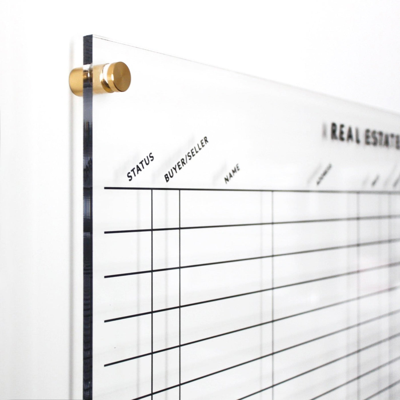 The Design Your Own Acrylic Tracking Board | Horizontal by Girl Friday Shop, featuring customizable gold metal hardware, grid lines, and columns for Status, Buyer/Seller, and Name, beautifully complements a white wall and is ideal for wet-erase markers.