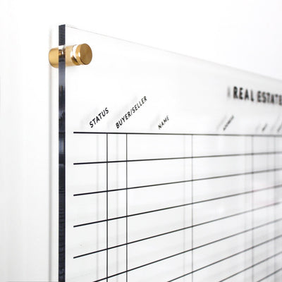 The Design Your Own Acrylic Tracking Board | Horizontal by Girl Friday Shop, featuring customizable gold metal hardware, grid lines, and columns for Status, Buyer/Seller, and Name, beautifully complements a white wall and is ideal for wet-erase markers.