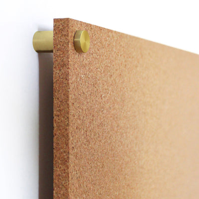 The Modern Cork Board with dots from Girl Friday Shop features a sleek, textured surface and is mounted using round gold-colored clips. Its design is perfect for customization with colorful push pins against a white background.