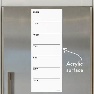 The Girl Friday Shops White Acrylic Dry Erase Weekly Calendar graces the metallic fridge door, with days listed vertically on the left. Its sleek design, text, and arrow make it a practical yet elegant addition to your kitchen space. No mounts needed!.