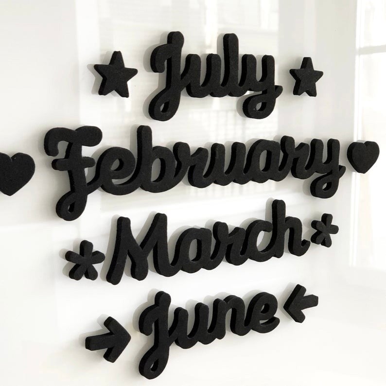The Girl Friday Shops Magnetic Month Words feature black cursive 3D text displaying July, February, March, and June on a white background, adorned with stars, hearts, and arrows, adding charm to any calendar setup.