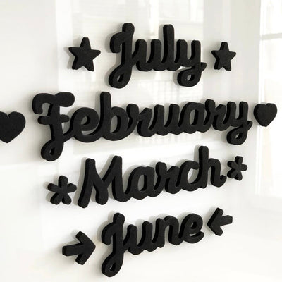 The Girl Friday Shops Magnetic Month Words feature black cursive 3D text displaying July, February, March, and June on a white background, adorned with stars, hearts, and arrows, adding charm to any calendar setup.
