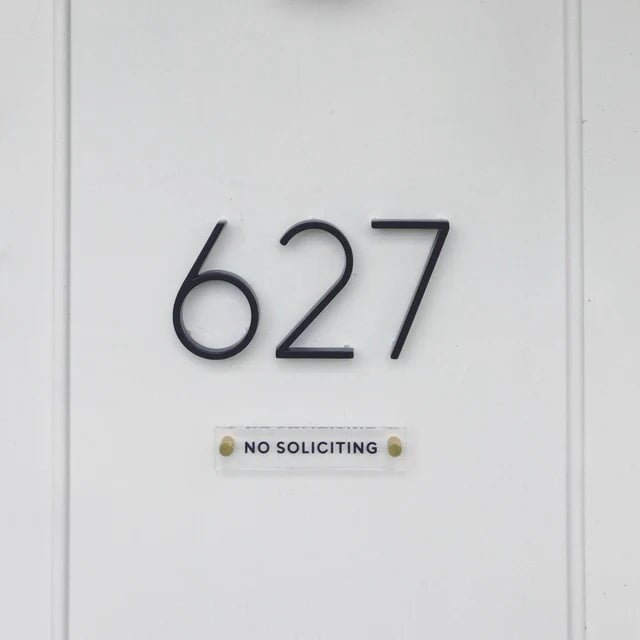 House number 627 is prominently shown in large black metal numbers on a white wall, with a small NO SOLICITING sign crafted from American-made acrylic by Girl Friday Shop below. Design your own custom text with the Design Your Own Acrylic Sign for a personalized touch.