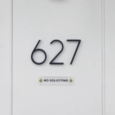 House number 627 is prominently shown in large black metal numbers on a white wall, with a small NO SOLICITING sign crafted from American-made acrylic by Girl Friday Shop below. Design your own custom text with the Design Your Own Acrylic Sign for a personalized touch.