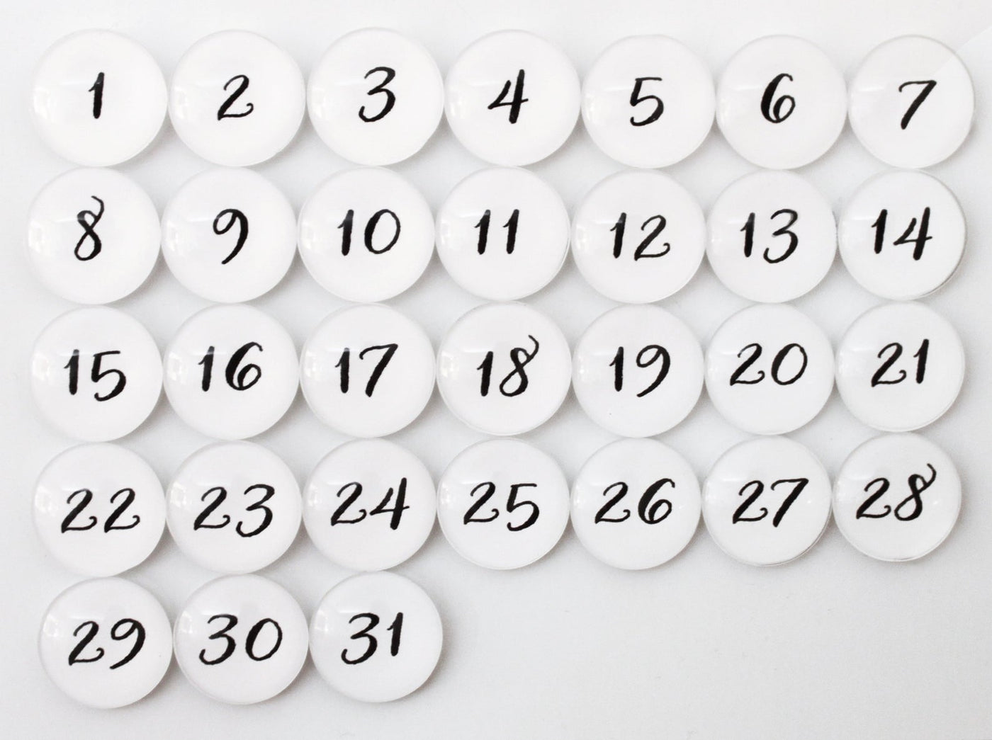 The Number Magnets - White by Girl Friday include 31 white glass magnets with black numbers from 1 to 31, arranged in four rows on a gray background to create a pop calendar effect.