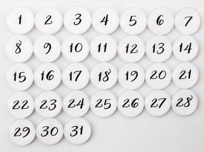 The Number Magnets - White by Girl Friday include 31 white glass magnets with black numbers from 1 to 31, arranged in four rows on a gray background to create a pop calendar effect.