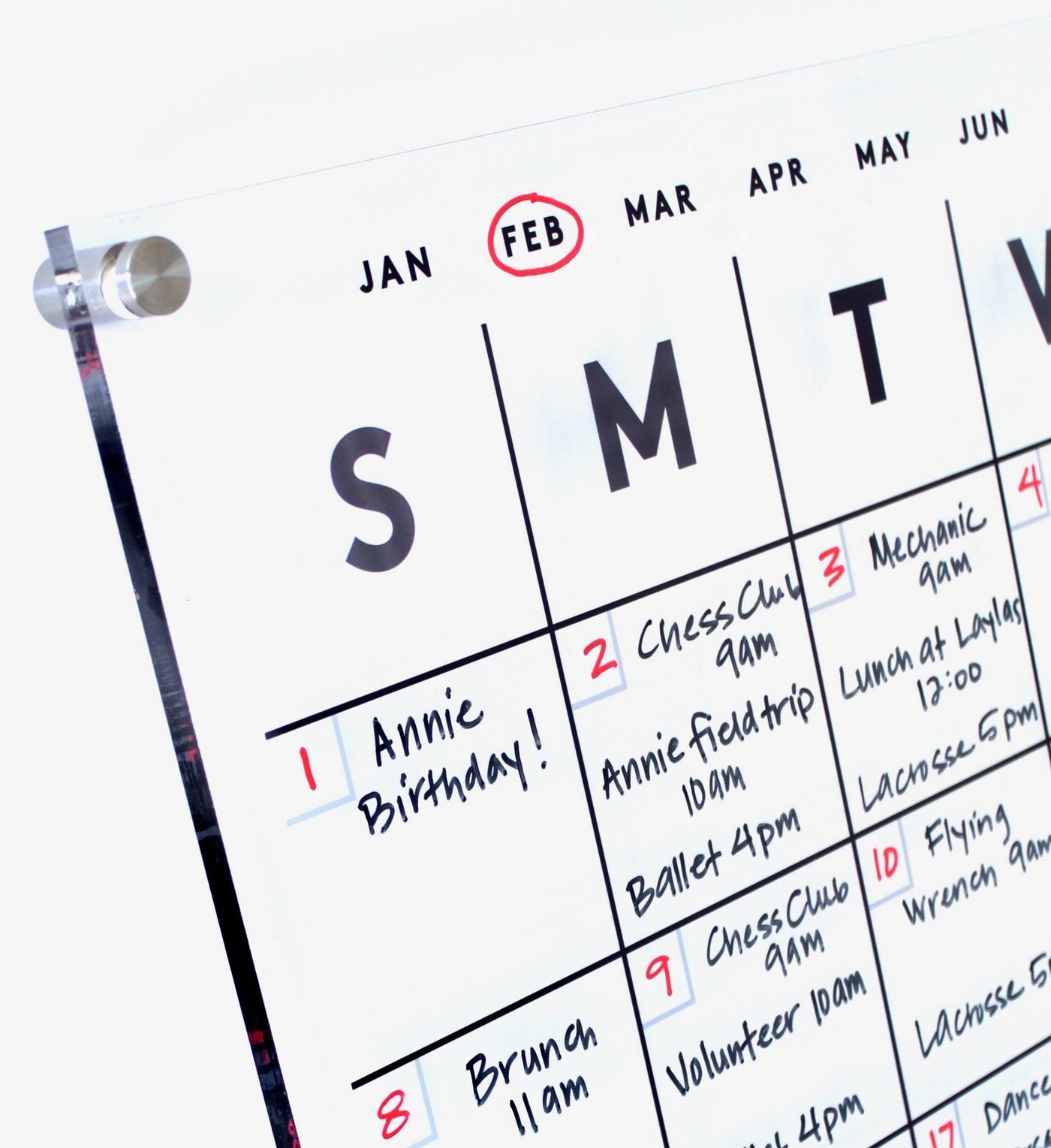 The Clear Acrylic Monthly Wall Calendar by Girl Friday showcases a high-quality finish with polished edges. In February, the 1st is marked for Annie Birthday!, and notes include events like a chess club meeting, field trip, and ballet practice for the week.