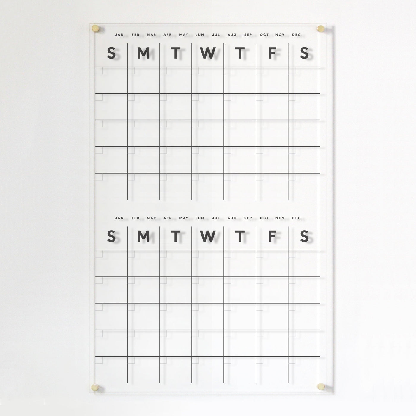 The Clear Acrylic Monthly Wall Calendar by Girl Friday, featuring polished edges and two sections, displays weekdays (S, M, T, W, T, F, S) with months from January to December listed above. It is crafted for a clean and modern design with high-quality materials.