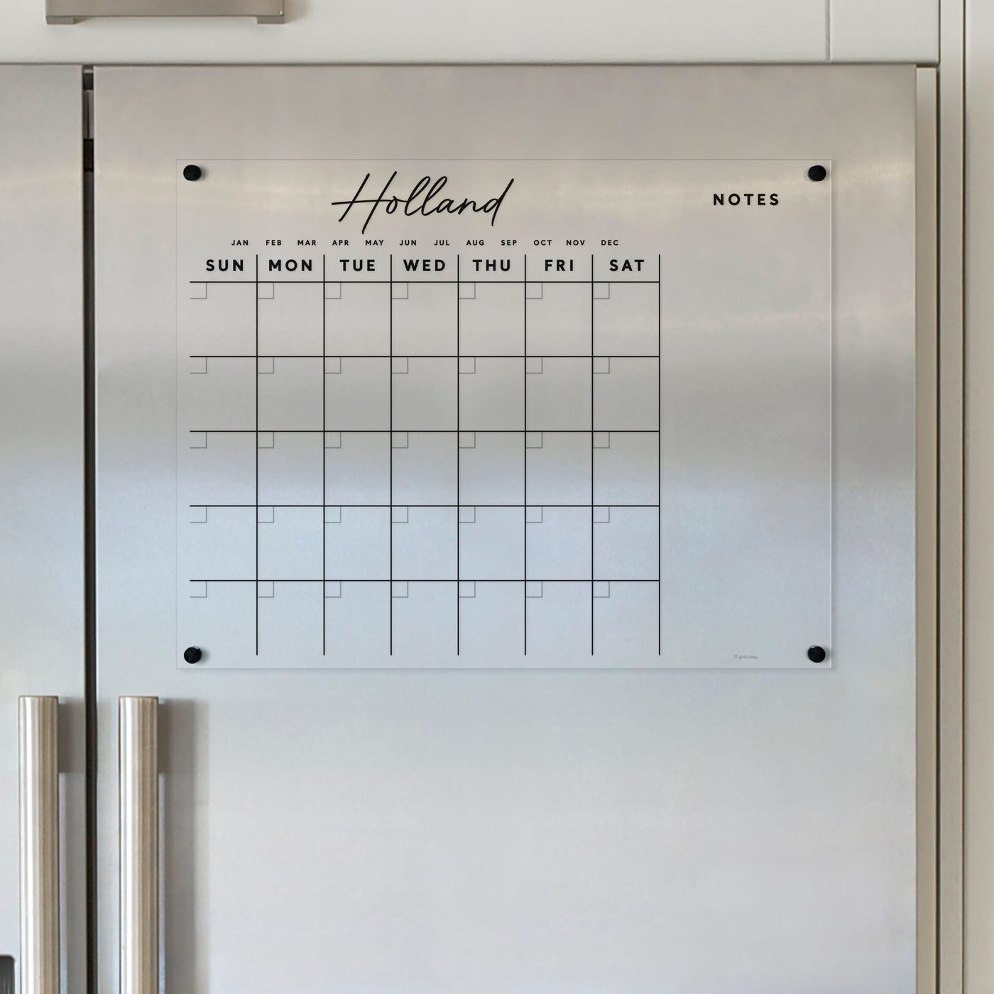The elegant Acrylic Fridge Calendar with Custom Family Name | Horizontal by Girl Friday features an acrylic wall mount, English days/months, weekly rows, and note space. Ideal above kitchen appliances with a white backdrop, its perfect for wet-erase markers.