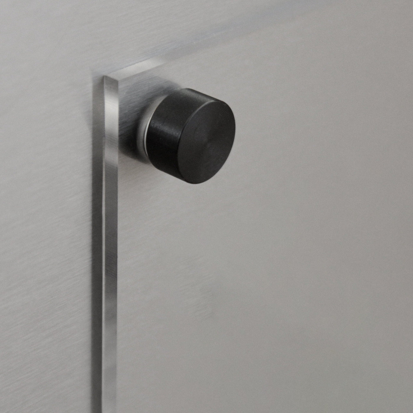 Close-up of a metallic door featuring a cylindrical black knob with space for the Girl Friday Clear Acrylic Fridge To Do List. The brushed metal texture enhances its modern look, and its perfect for wet-erase markers to boost its minimalist functionality.