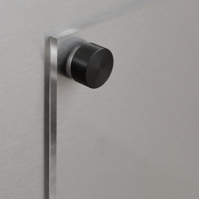 Close-up of a metallic door featuring a cylindrical black knob with space for the Girl Friday Clear Acrylic Fridge To Do List. The brushed metal texture enhances its modern look, and its perfect for wet-erase markers to boost its minimalist functionality.