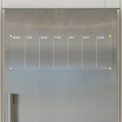 The Girl Friday Acrylic Fridge Calendar weekly is a modern and minimalist clear acrylic calendar with a magnetic surface, featuring columns labeled MON-SUN. Its perfect for wet-erase markers and fits stylishly on your stainless steel fridge.