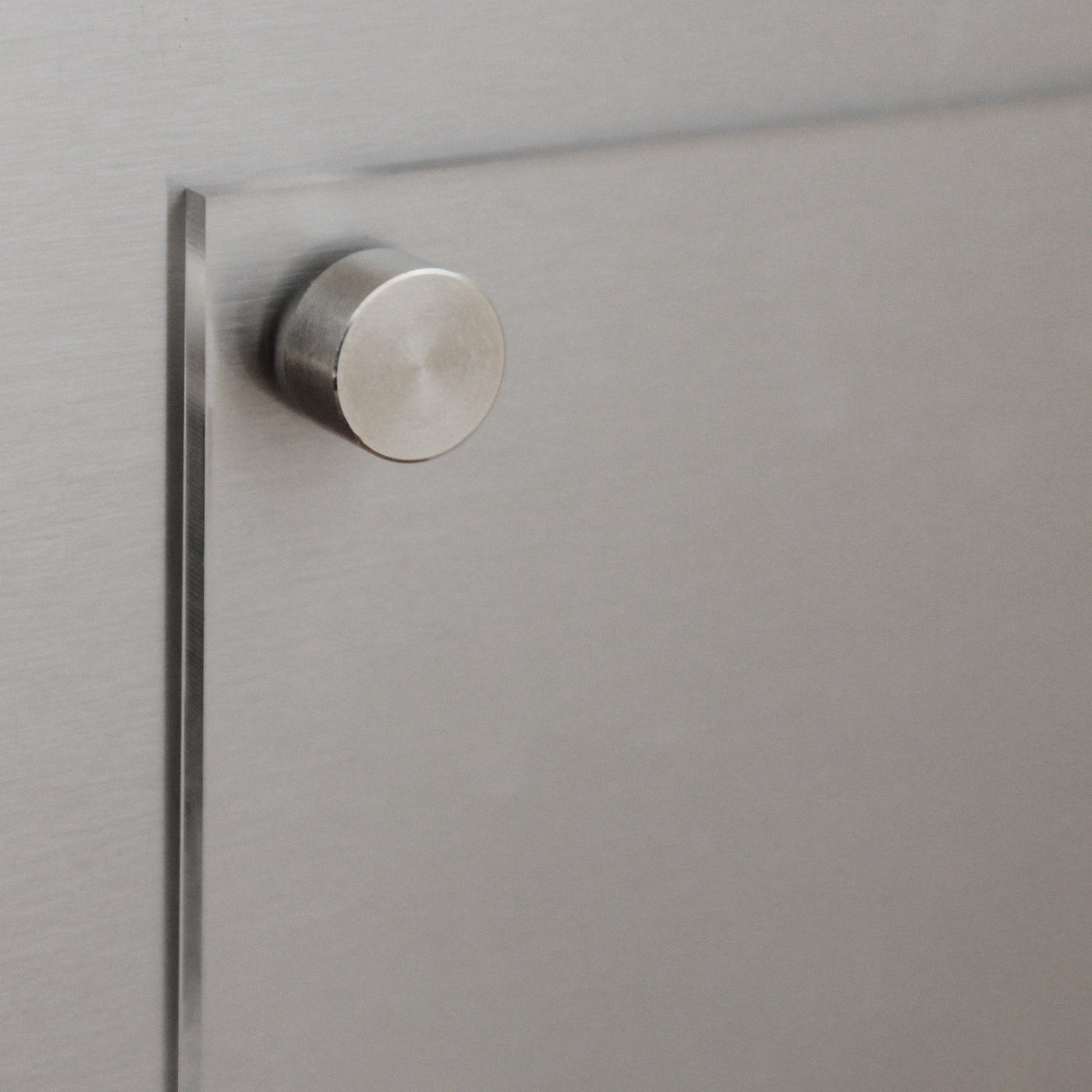 A close-up of a metallic drawer features a round, brushed metal knob reflecting soft light. Its sleek, modern design complements the customizable Clear Acrylic Fridge To Do List by Girl Friday, emphasizing texture and finish.