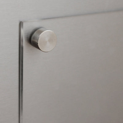 A close-up of a metallic drawer features a round, brushed metal knob reflecting soft light. Its sleek, modern design complements the customizable Clear Acrylic Fridge To Do List by Girl Friday, emphasizing texture and finish.