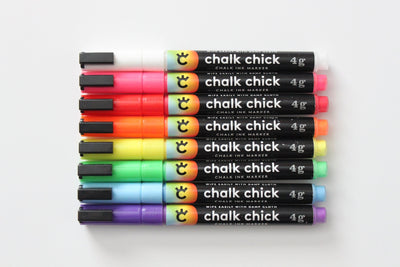 Eight vibrant chalk chick markers, featuring white, red, orange, pink, green, blue, light blue, and purple hues with sleek black caps and labeled text, are ideal for wet-erase use or pairing with the Girl Friday Clear Acrylic Fridge Calendar.