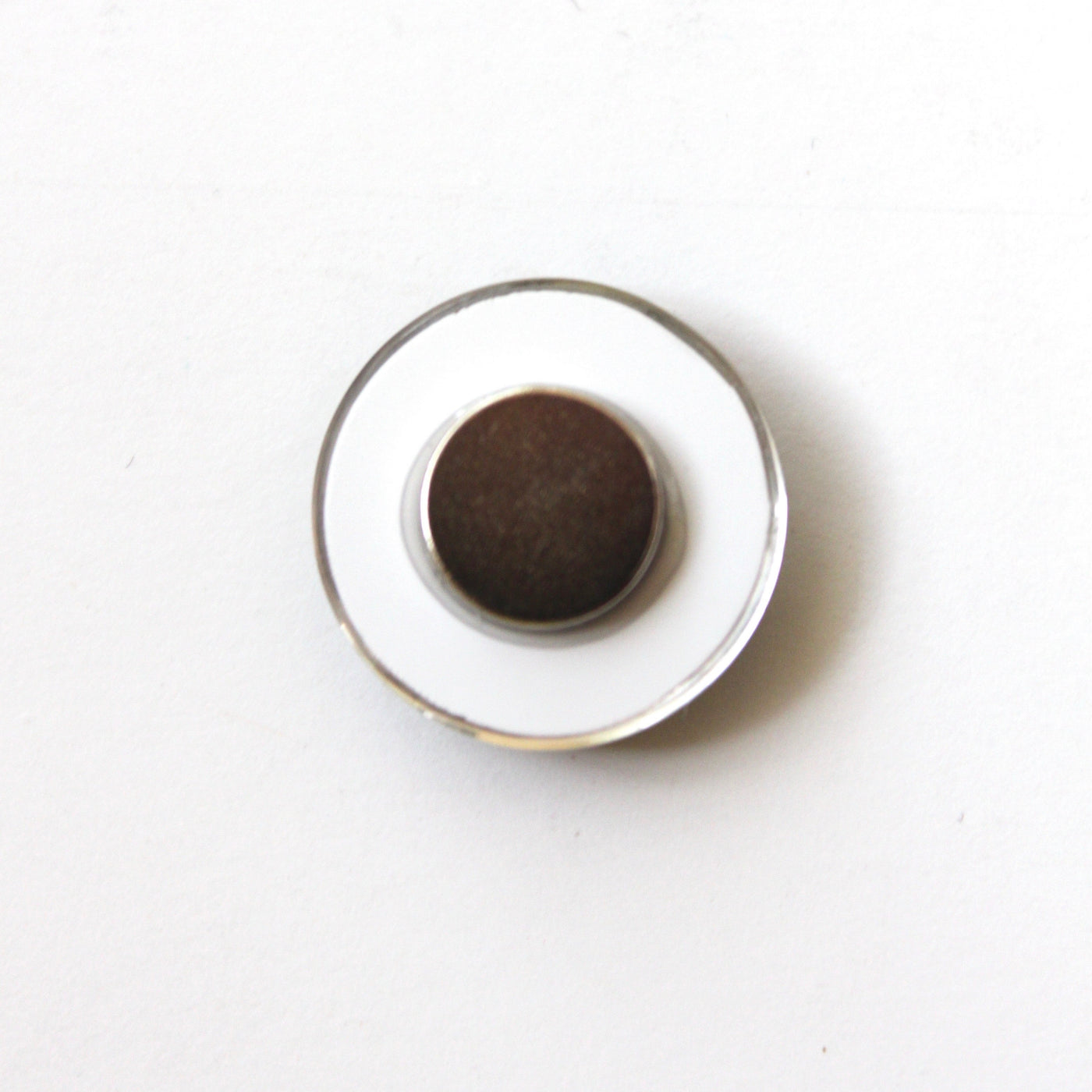 Against a plain, light backdrop sits a Girl Friday Number Magnet, capturing simplicity with its small, round shape featuring a dark center and white base.
