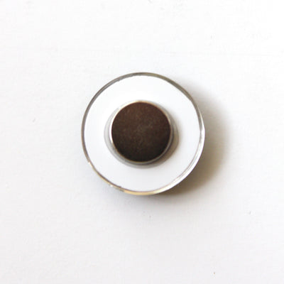 Against a plain, light backdrop sits a Girl Friday Number Magnet, capturing simplicity with its small, round shape featuring a dark center and white base.