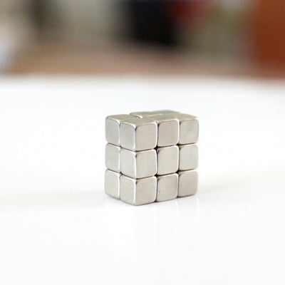 A small 3x3 grid of neodymium cube magnets is arranged on a sleek, white surface using Girl Fridays metal strips designed to hold them, creating a gleaming structure against a blurred backdrop.