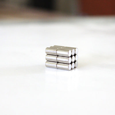 A stack of Girl Friday Shops Strong magnets, with a metallic silver finish, is arranged in a rectangular block on a smooth white surface, neatly aligning the cylindrical magnets in rows.