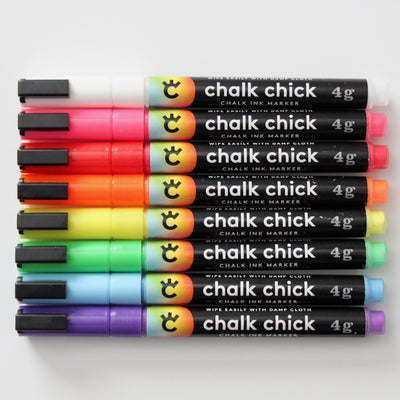 Set of 8 Chalk Chick ink markers in vibrant colors: white, red, pink, orange, yellow, green, blue, and purple. Ideal for use as wet-erase markers on the Girl Friday Clear Acrylic Fridge Calendar Menu Board. Features sleek black labels with brand logo and description.