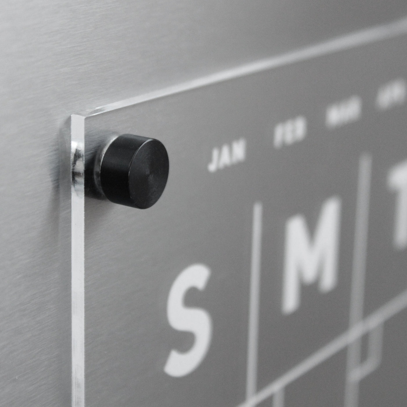 A large-lettered modern wall calendar perfect as a fridge calendar. With JAN in small letters and S, M, T for weekdays, this Clear Acrylic Monthly Fridge Calendar by Girl Friday Shop mounts magnetically with a black peg.