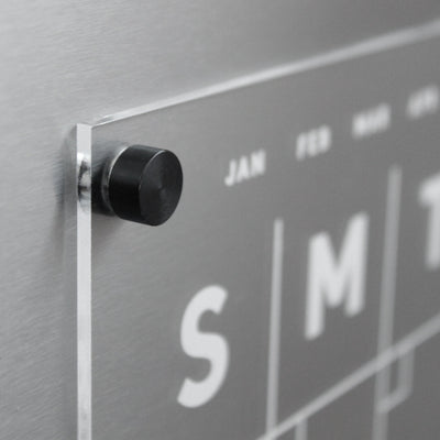 A large-lettered modern wall calendar perfect as a fridge calendar. With JAN in small letters and S, M, T for weekdays, this Clear Acrylic Monthly Fridge Calendar by Girl Friday Shop mounts magnetically with a black peg.